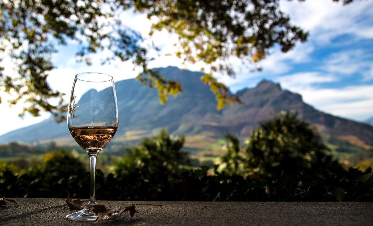 Ein Glas mit Rosé-Wein auf einer Mauer, im Hintergrund sieht man einen Berg