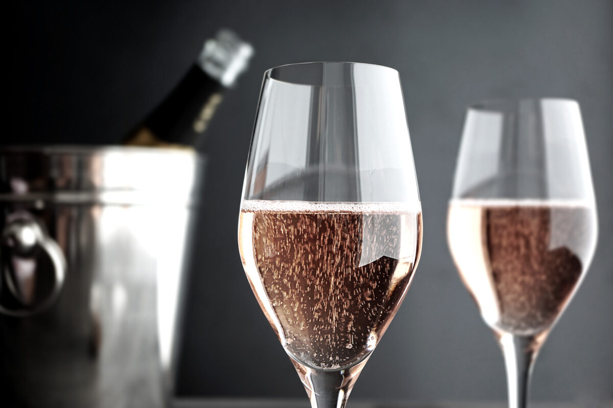 Zwei Gläser mit Rosé-Champagner - im Hintergrund die Schaumweinflasche in einem Kühler