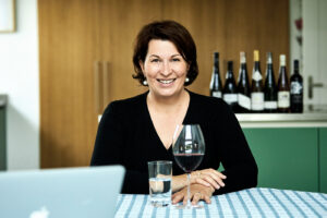 Master of Wine Romana Echensperger an einem Tisch mit einem Glas Rotwein und einem Wasserglas sitzend.