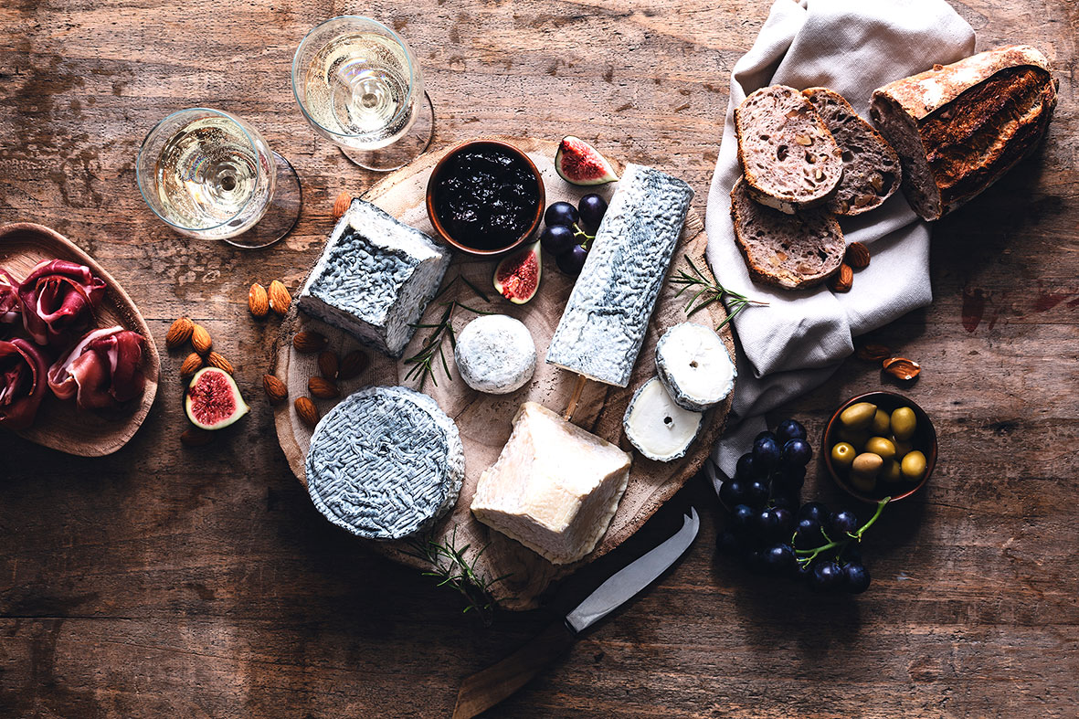 Käse und Wein hübsch auf einem Holztisch dekoriert mit Brot, Schinken und Oliven dazu