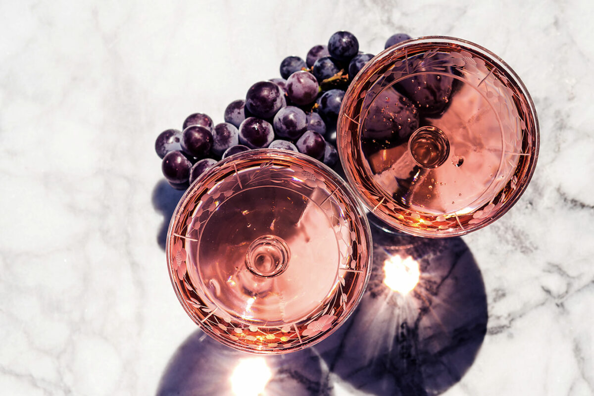 Zwei Gläser mit Rosé-Wein auf einem Marmortisch im Sonnenlicht, daneben rote Trauben