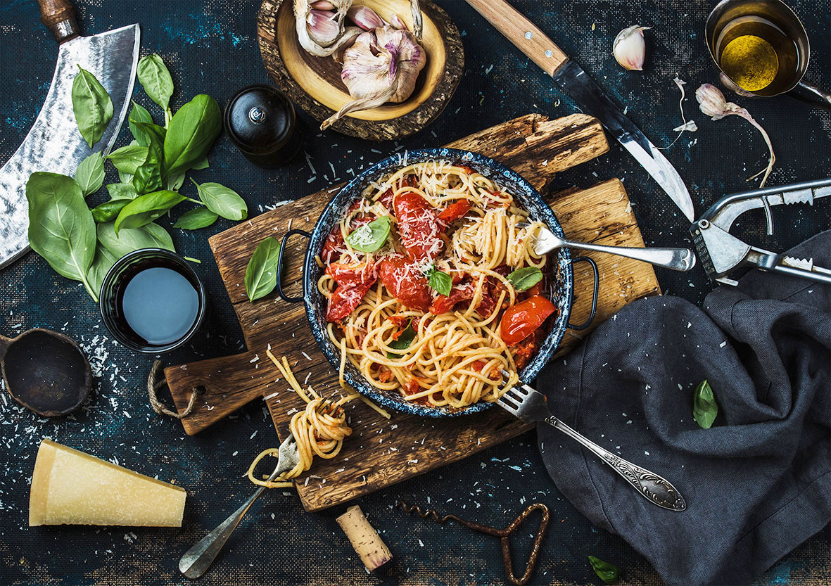 Spaghetti mit Tomaten auf einem Teller und ganz vielen Lebensmitteln drum herum aus der Vogelperspektive fotographiert