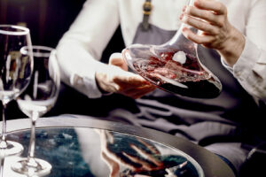 Sommelier schwenkt Rotwein in einem Dekanter - vor ihm stehen leere Weingläser