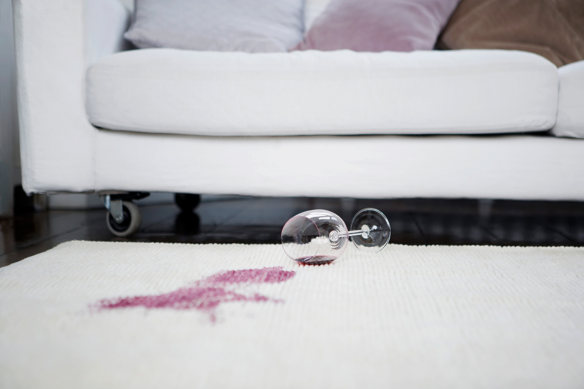 Umgekipptes Rotweinglas samt Rotweinfleck auf einem weißen Teppich